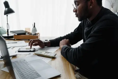 Man Sitting At Desk With Calculator And Laptop